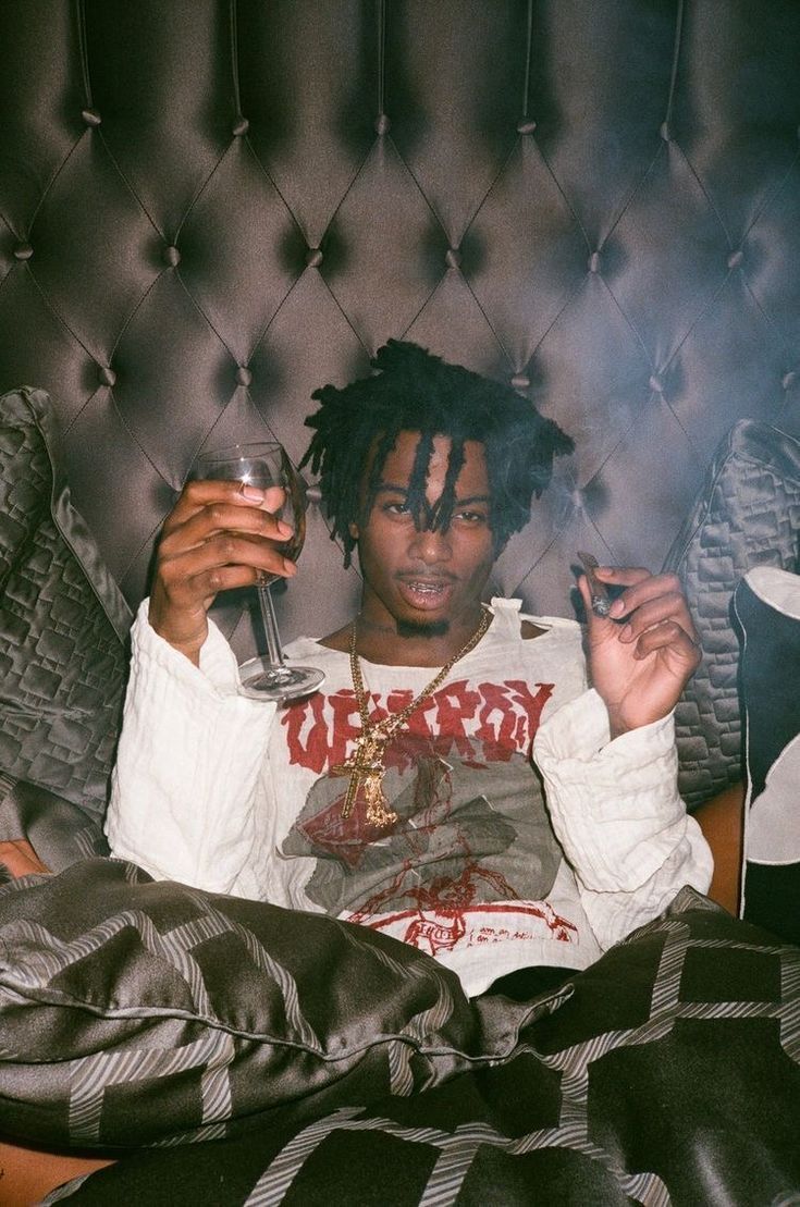 a man with dreadlocks sitting on a bed holding a glass in his hand