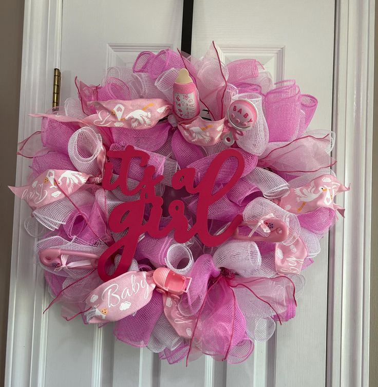 a pink mesh wreath with the word girl on it hanging on a white front door