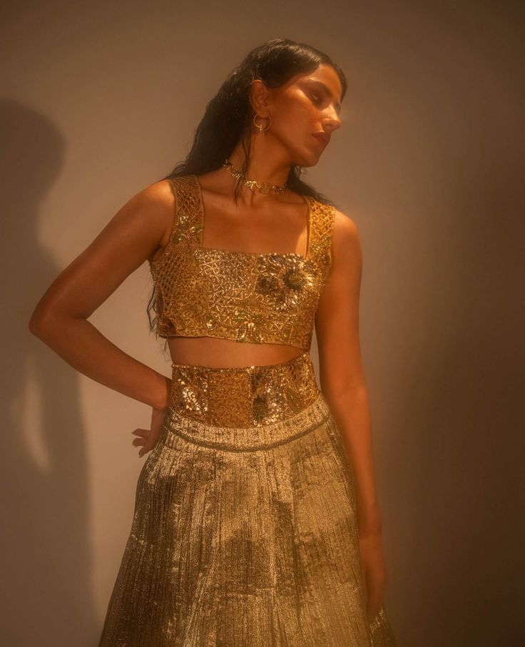 Step into refined elegance with the goldusion ensemble, where traditional craftsmanship meets modern innovation. The metallic lehenga, crafted from hand-crushed gold fabric, exudes opulence, while the detachable corset belt and blouse are fully embellished for added glamour. Architectural embroidery, inspired by mughal lattice motifs, adds a striking, textured dimension. A masterful fusion of texture, form, and cultural heritage, this ensemble redefines contemporary sophistication. Metallic Lehenga, Architectural Embroidery, Lehenga And Blouse, Corset Belt, Gold Fabric, Cultural Heritage, Photographic Lighting, Traditional Techniques, Lattice