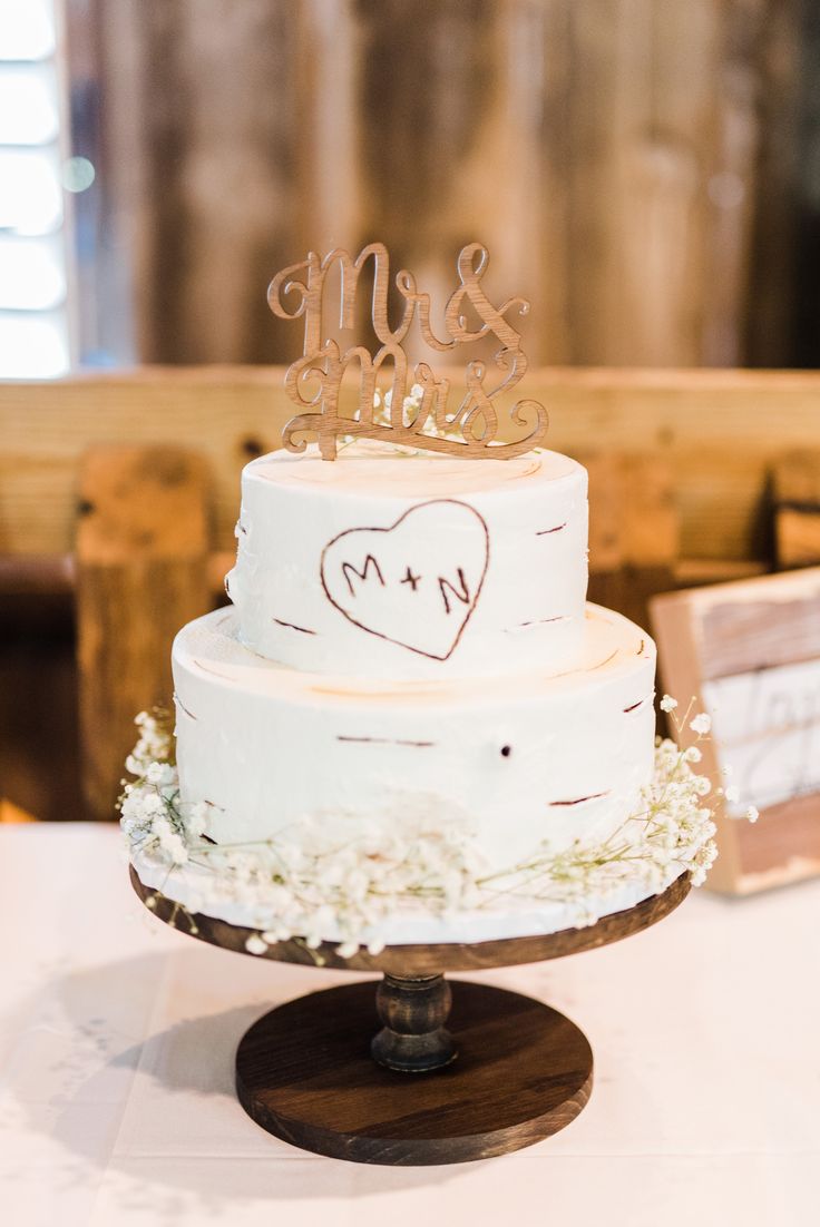 a white wedding cake sitting on top of a wooden table next to a couple's initials