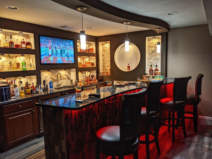 a bar with several stools in front of it and television screens on the wall