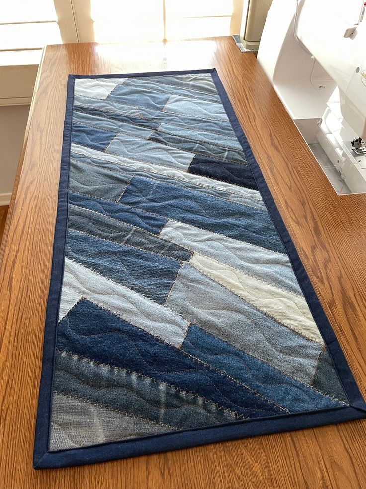 a wooden table with a blue patchwork rug on it and sewing machine in the background