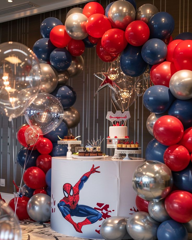 a table with balloons, cake and cupcakes on it at a spiderman birthday party