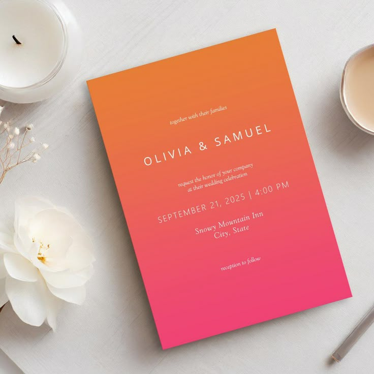 an orange and pink wedding card sitting on top of a table next to some flowers