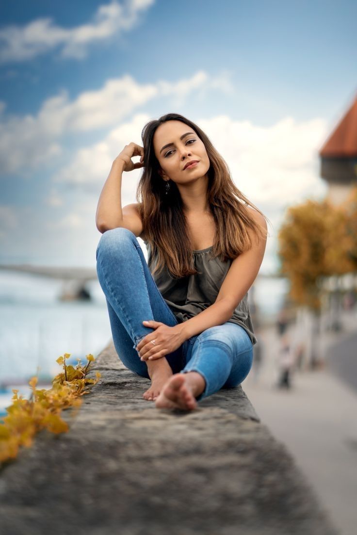 a woman is sitting on the edge of a wall with her hands behind her head