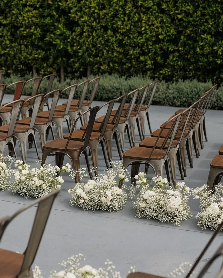 rows of wooden chairs with white flowers on the floor in front of trees and bushes