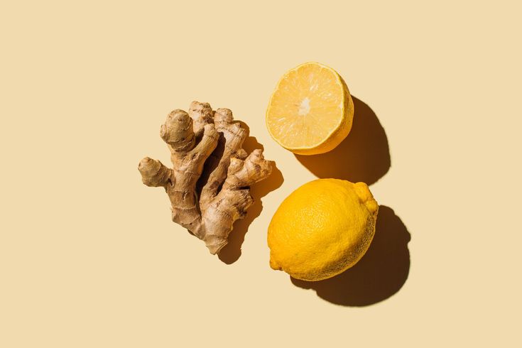 two lemons, ginger and ginger root on a yellow background with shadow from the top