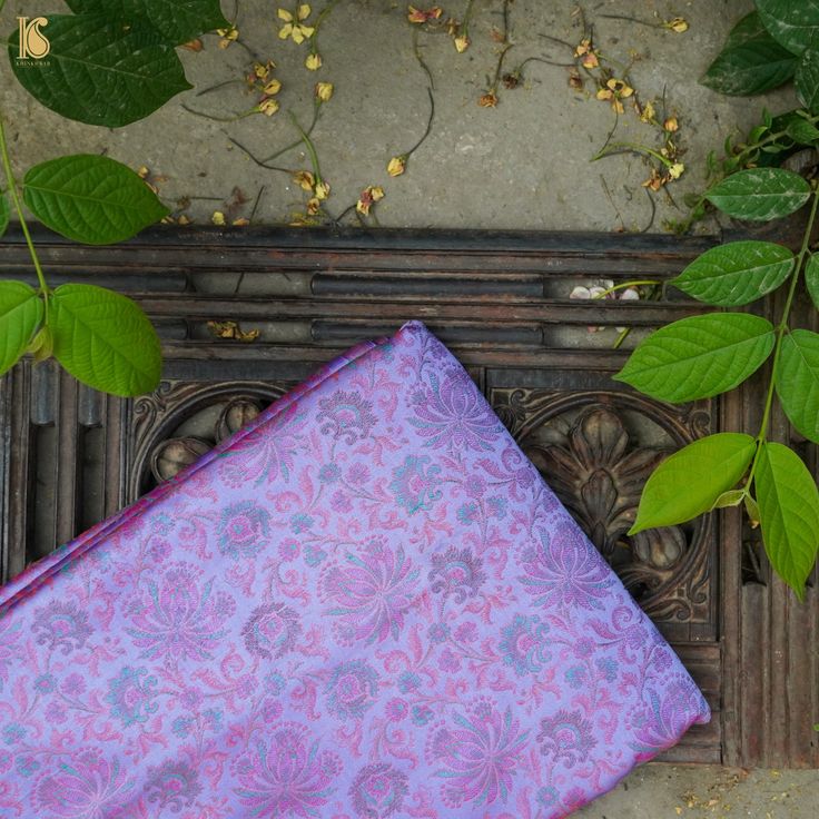 a purple and blue cloth sitting on top of a wooden bench next to green leaves