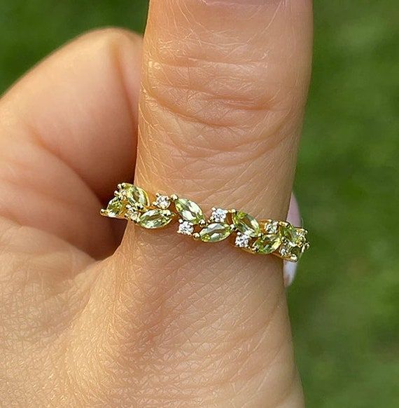 a woman's hand holding a ring with green and white stones on the side