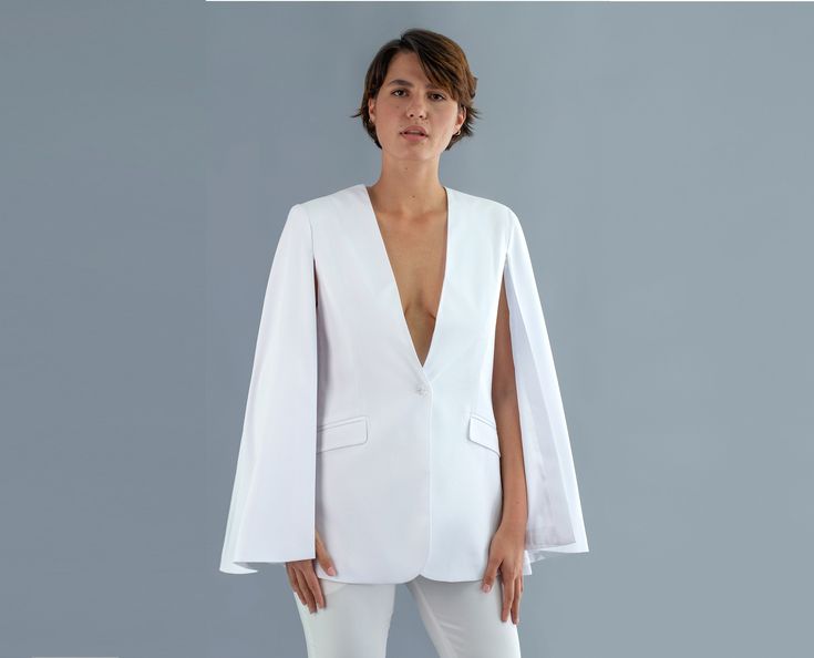 Idyllic presents a stylish, high quality cape blazer, perfect for events or civil union. This blazer is elegant and very comfortable. It is made out of taffeta and has flap pockets. Due to its sophisticated nature and white color, this blazer is ideal for a special occasion like a civil union. The model is fully lined. Composition: blazer - 80% polyester, 20% elastane; satin lining: 100% polyester. Delivery time: 1-2 weeks. The product can be adjusted based on the client's silhouette and style. Feel free to contact us with anything you have in mind! Luxury Asymmetrical Blazer For Semi-formal Occasions, Luxury Asymmetrical Blazer For Formal Occasions, Luxury White Blazer For Festive Season, Luxury Winter White Formal Blazer, Luxury Elegant White Blazer, Luxury Classic Off White Blazer, Luxury Asymmetrical Blazer For Party, Luxury White Blazer For Workwear, Luxury White Single Breasted Blazer