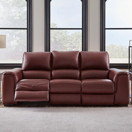 a red leather reclining sofa in front of three windows with two lamps on either side