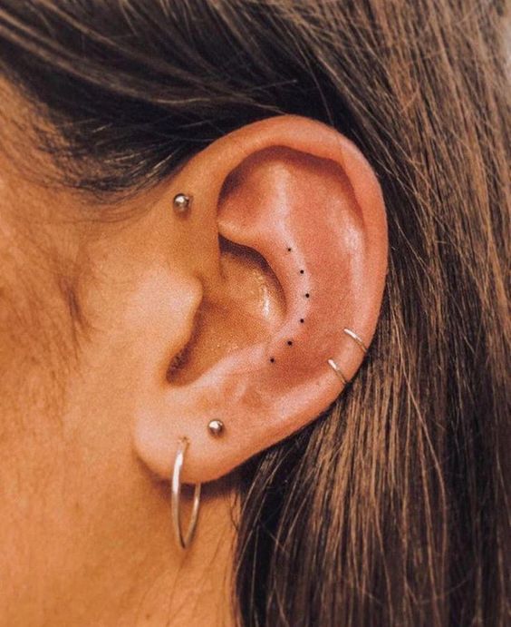 a woman's ear with small black dots on the middle part of her left ear