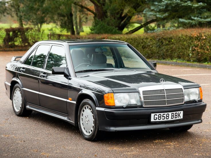 a black mercedes benz parked in a parking lot next to trees and bushes on either side of the road