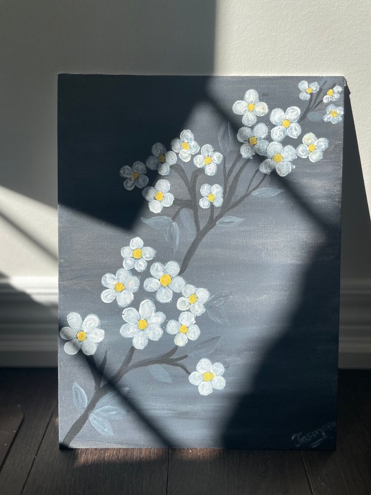 a painting with white and yellow flowers painted on it's side, sitting on a wooden floor