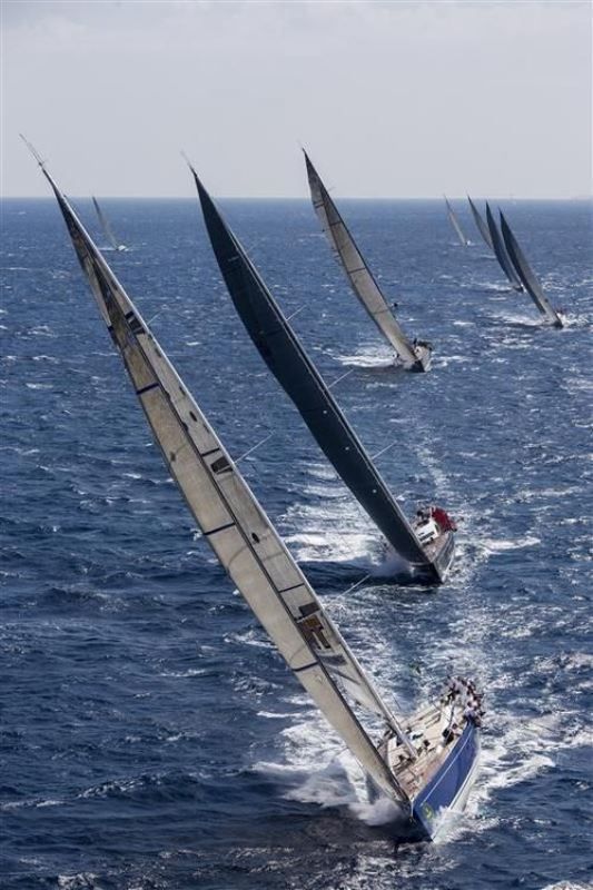 several sailboats are sailing in the open ocean water, one is blue and white