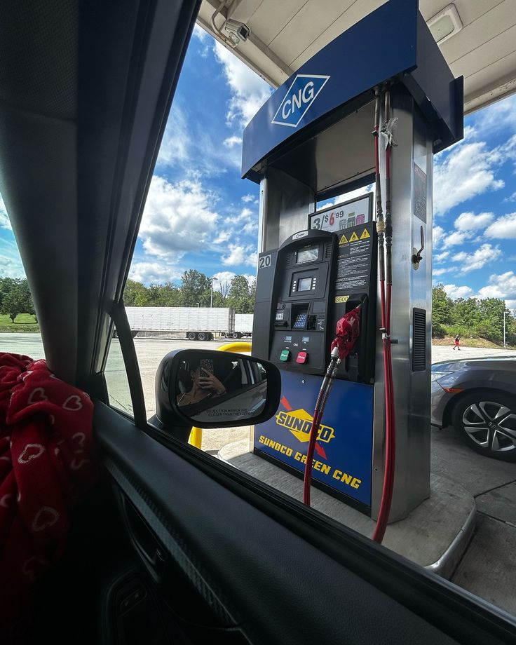 a gas pump is seen through the side window of a car at a gas station