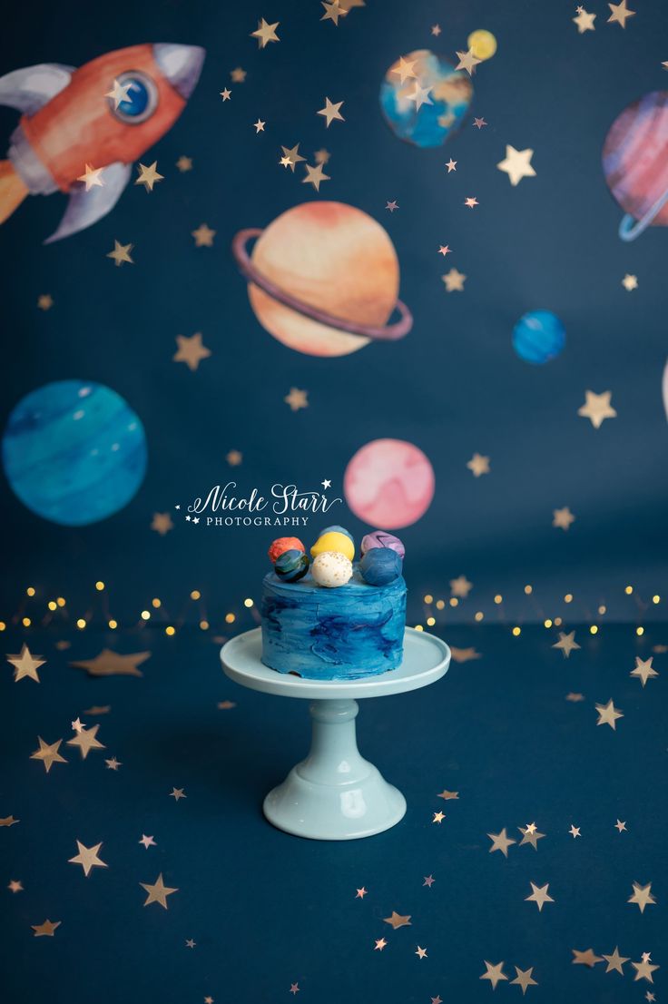 a space themed cake with planets and stars on the wall behind it is sitting on a pedestal in front of a blue backdrop