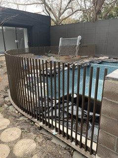 a fence that has been placed next to a swimming pool in a backyard with rocks and gravel on the ground