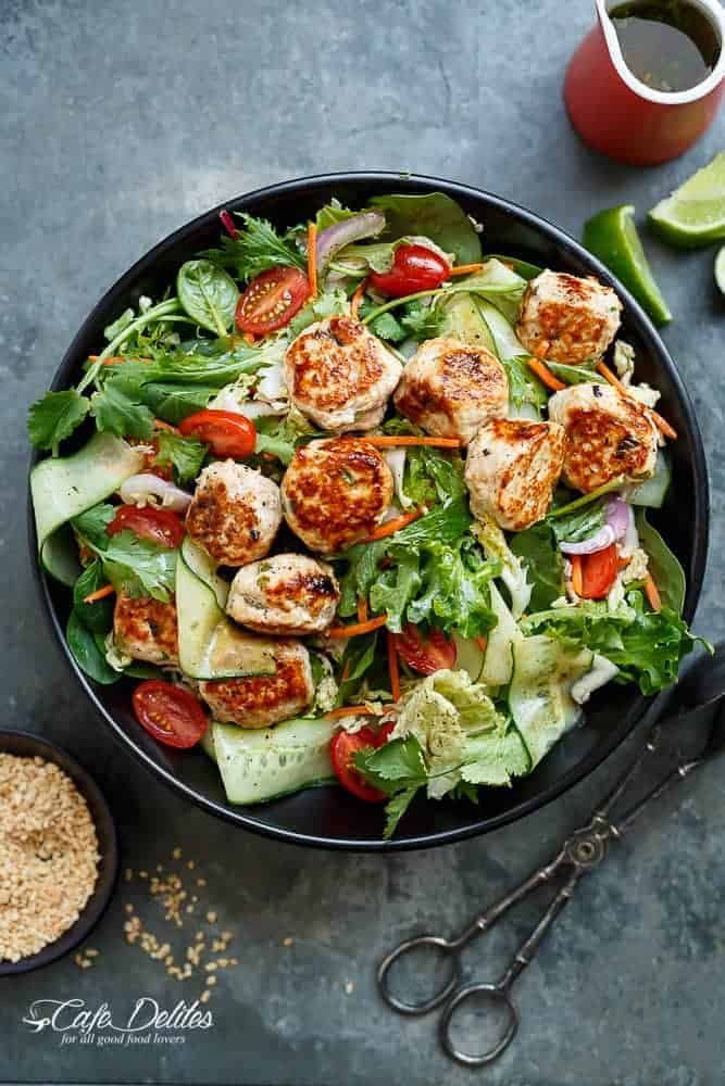 a salad in a bowl with meat and veggies next to some seasoning