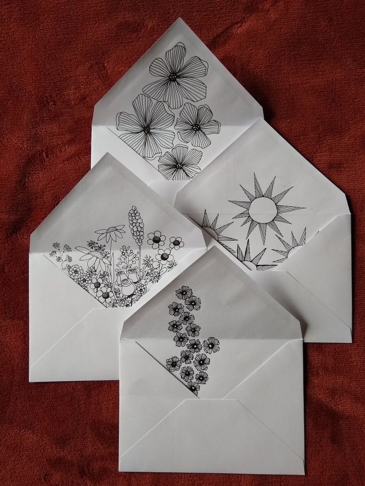 four envelopes with designs on them sitting on a red cloth covered tablecloth in the shape of flowers