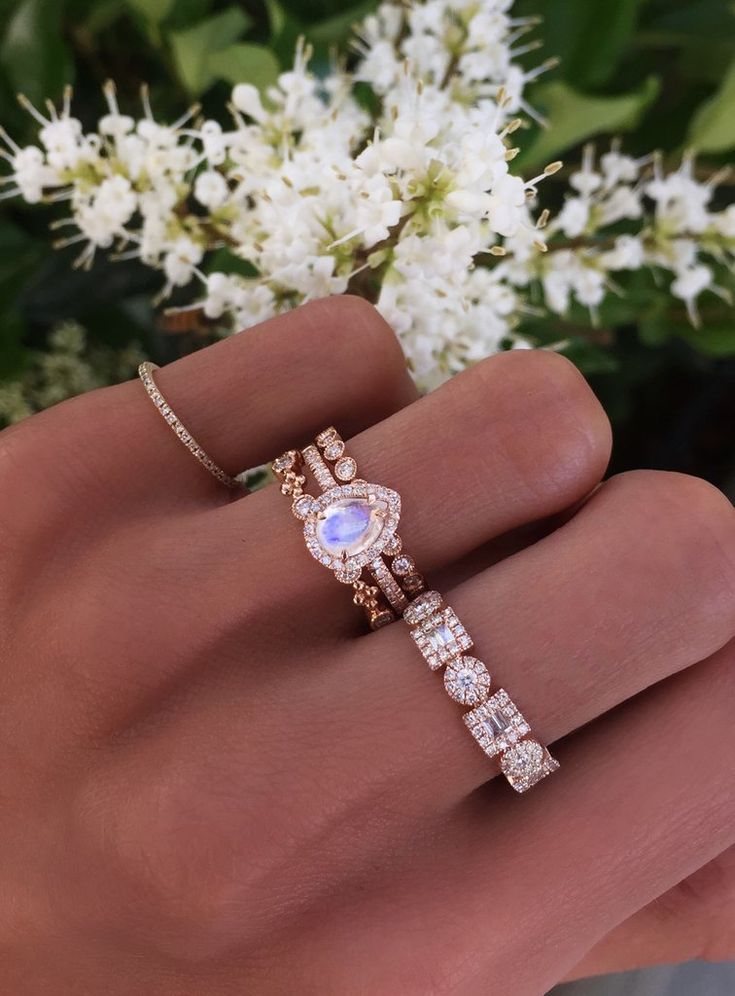 a woman's hand holding a ring with an oval shaped stone and diamond band