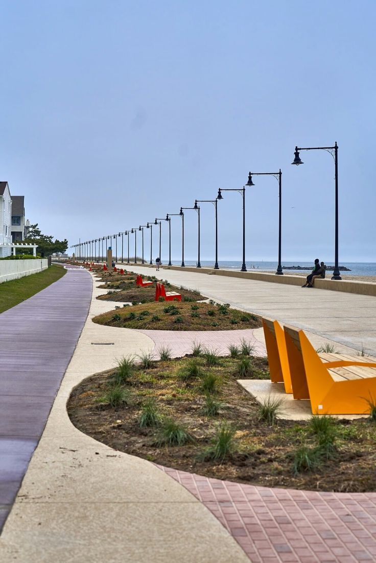 an empty sidewalk next to the ocean with benches on each side and street lights in the background