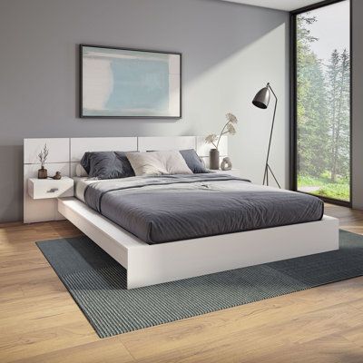 a large bed sitting on top of a hard wood floor next to a tall window