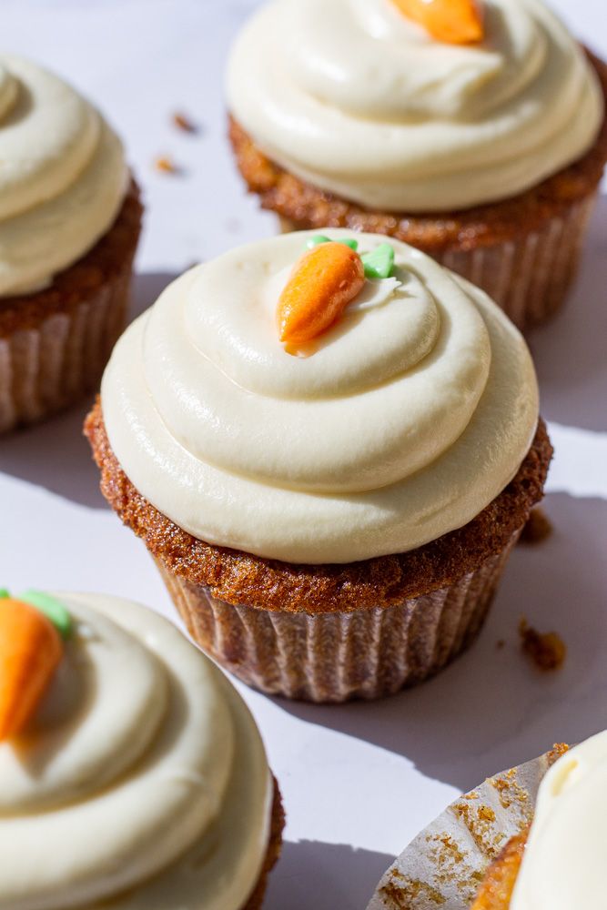 cupcakes with frosting and carrots on them sitting on a white surface