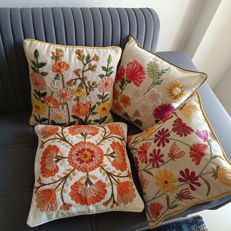 four decorative pillows on a couch in a living room with a blue chair and wall behind them