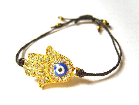 A cute string bracelet featuring the Hand of Fatima.This pretty gold plated charm depicts an open palm, the Hand of Fatima.  Known in some cultures as the Hamsa, the Hand Of Fatima is thought to provide protection and good luck to those who carry it with them!This particular charm has little diamantes set within it and also features the evil eye symbol.The charm is suspended on a black, 100% cotton cord which has been tied in such a way as to have an adjustable fastening.  Slip the bracelet over Adjustable Symbolic Gold Beaded Bracelets, Gold Braided Bracelet With Evil Eye For Gift, Gold Braided Bracelet With Evil Eye As Gift, Gold Braided Evil Eye Bracelet As A Gift, Symbolic Adjustable Friendship Charm Bracelet, Adjustable Gold Charm Bracelet With Evil Eye, Gold Evil Eye Bracelet With Adjustable Length As Gift, Adjustable Gold Evil Eye Symbolic Bracelet, Gold Adjustable Evil Eye Bracelet