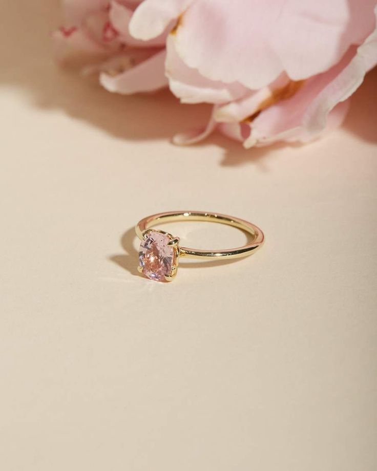 a pink diamond ring sitting on top of a table next to some flowers and petals