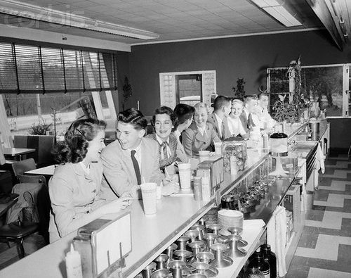 an old black and white photo of some people at a diner with cups on the counter