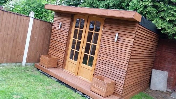 a wooden shed sitting in the grass next to a fence