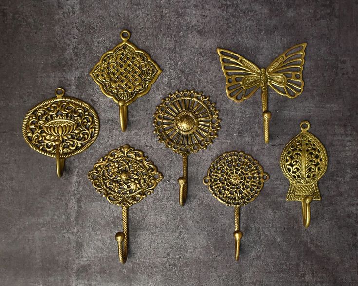 six antique brass - plated wall hooks, including one with a butterfly on it