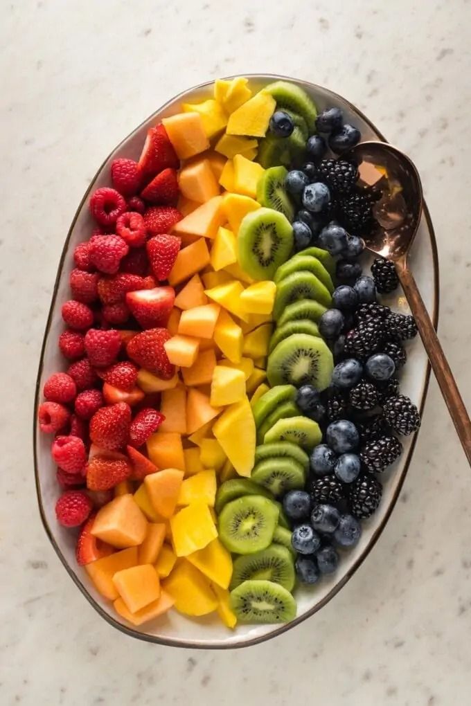 a plate filled with sliced fruit on top of a white marble counter next to a spoon