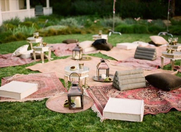 an outdoor seating area is set up on the grass with lanterns and rugs around it