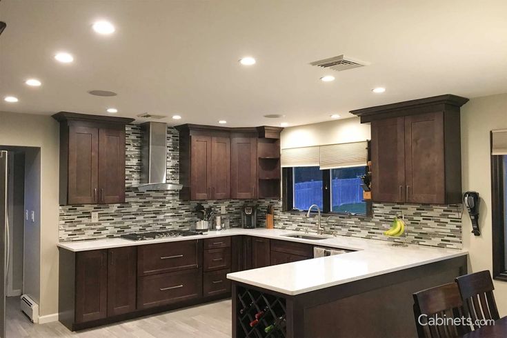 a kitchen with dark wood cabinets and white counter tops is shown in this image, there are lights on the ceiling