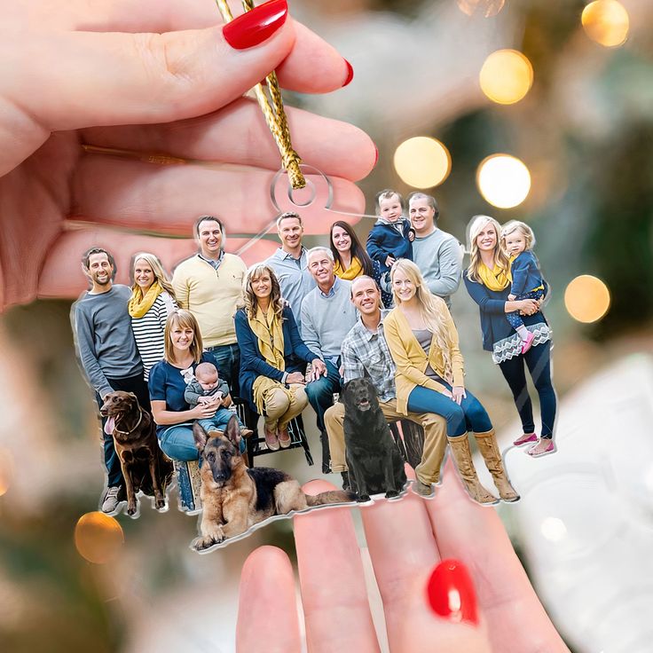 a hand holding a christmas ornament with a group of people and a dog on it