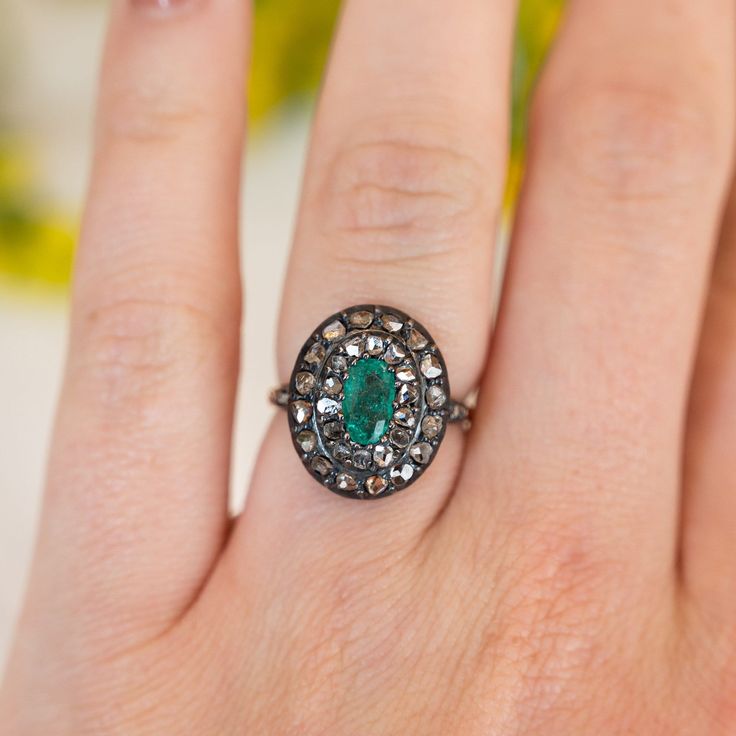 This antique Georgian ring features a .72 carat emerald and accent diamonds in two-tone 14 karat yellow gold and sterling silver. The oval cut emerald has a green-blue hue and is prong set in the center of an oval mounting. Thirty (30) accent diamonds halo the center emerald with six (6) accent diamonds decorating the shoulders of the band, set in sterling silver. From the profile, an openwork basket mounting holds the collection of gemstones finished on a polished and engraved 14 karat yellow g Oval Emerald Ring With Single Cut Diamonds, Heirloom Emerald-cut Ring With Single Cut Diamonds, Heirloom Emerald Cut Ring With Single Cut Diamonds, Oval Green Rose Cut Diamond Rings, Oval Emerald Ring With Rose Cut Diamonds, Heirloom Oval Emerald Ring With Single Cut Diamonds, Oval Emerald Ring With Single Cut Diamonds For Anniversary, Green Oval Diamond Ring With Single Cut, Heirloom Oval Emerald Ring With Rose Cut Diamonds