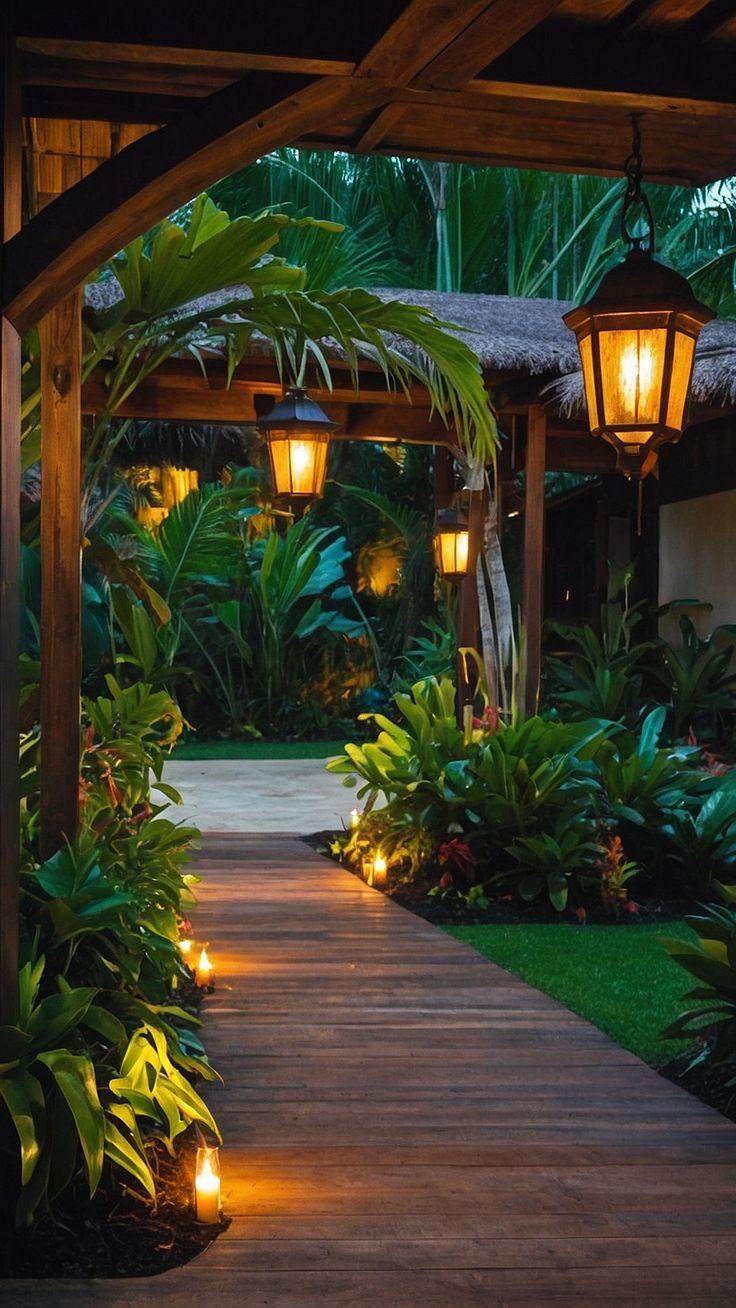 an outdoor walkway lit up with lanterns and greenery at night, surrounded by palm trees