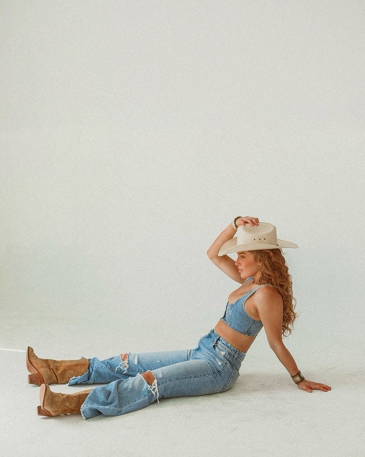 a woman in jeans and a cowboy hat laying on the ground