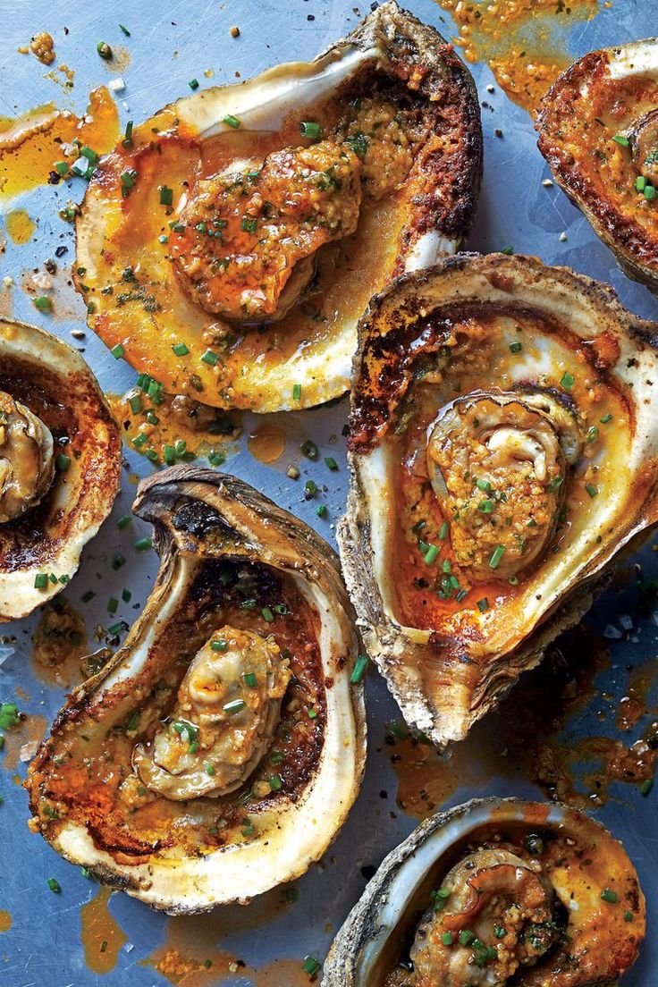 several oysters on a blue surface with parsley and seasoning sprinkled around them