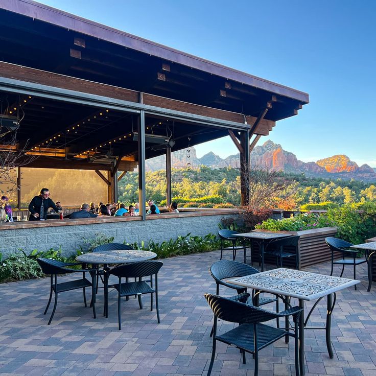 an outdoor dining area with mountains in the background and people sitting at tables on the patio