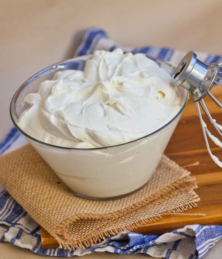 whipped cream in a glass bowl next to a whisk on a wooden board