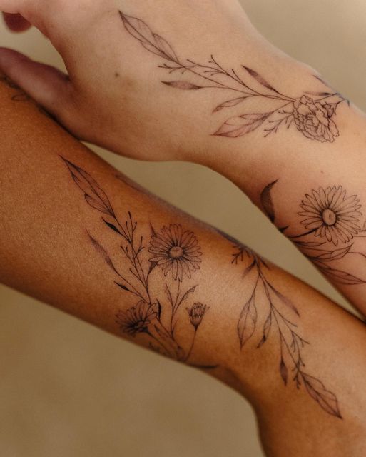 two people with tattoos on their arms holding each other's hands, one has a flower and the other has leaves