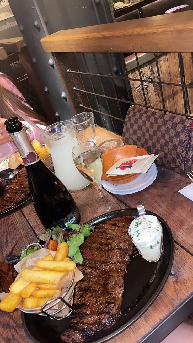 steak and fries on a table at a restaurant with drinks in front of it, along with other food items