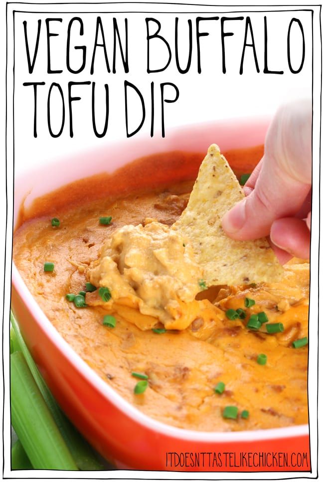 a hand dipping a tortilla chip into a bowl of vegan buffalo tofu dip