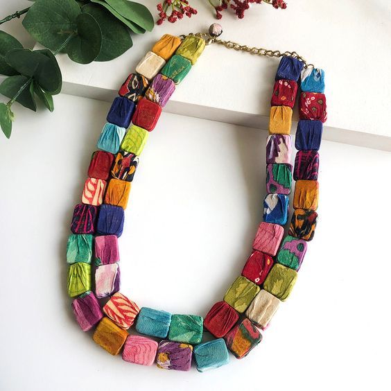 a multicolored necklace on a white surface next to some flowers and greenery