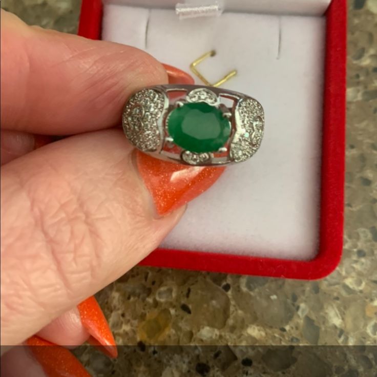 a woman's hand holding an emerald and diamond ring in a red velvet box