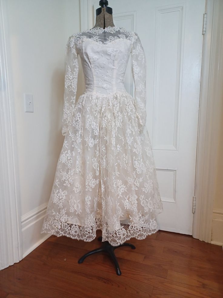 a white dress on a mannequin stand in front of a door with a wooden floor